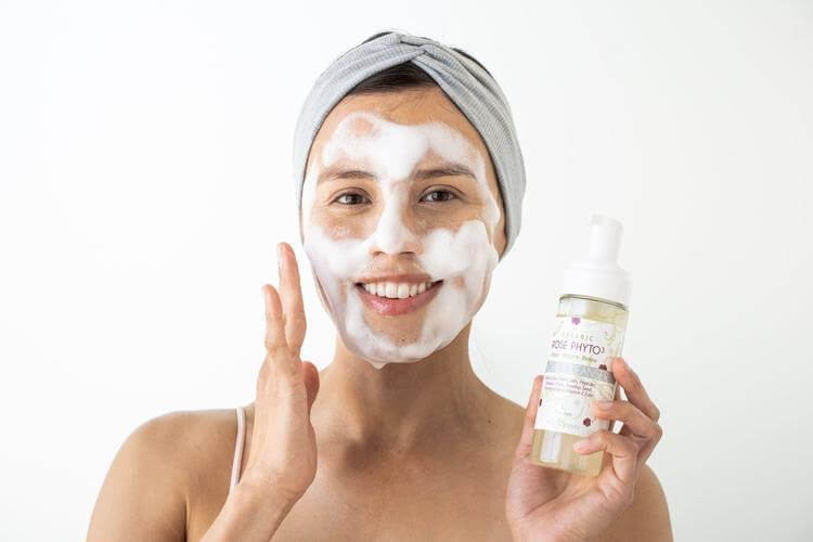Organic Rose Phyto Facial Cleanser 5 ounces being held in a woman's hand while she happily uses the cleanser on her face.