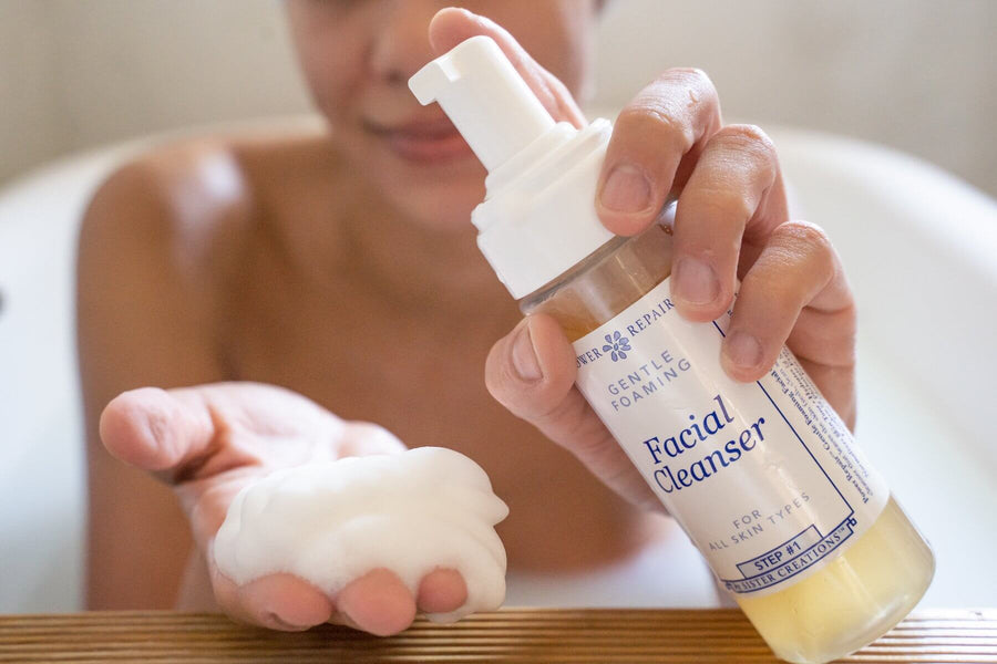 A woman in a bath tub pumps a bottle of foaming Power Repair Skin Cleanser by Sister Creations into her hand. It is very foamy.