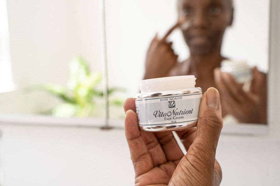A beautiful black woman is applying the Vita Nutrient Face Cream to her face while holding the container in her hand.