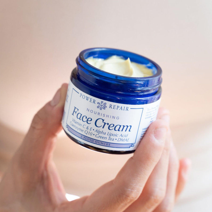 A woman holds an open 2 fl. oz. glass jar of Power Repair Face Cream By Sister Creations