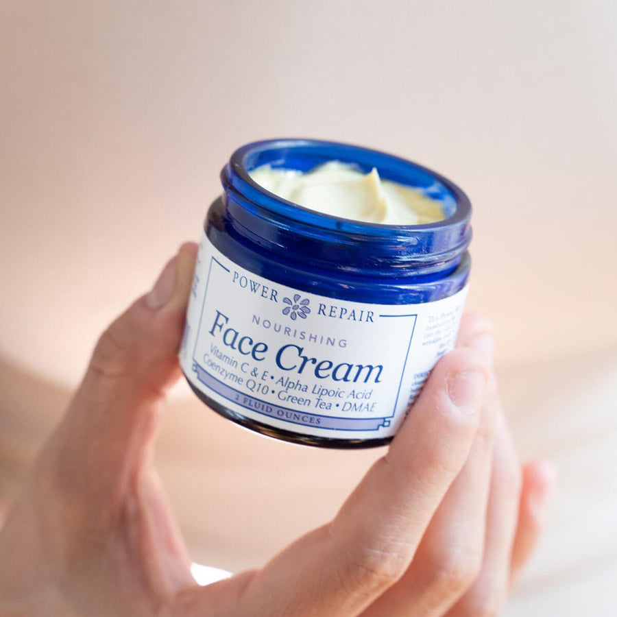 A woman holds an open 2 fl. oz. glass jar of Power Repair Face Cream By Sister Creations