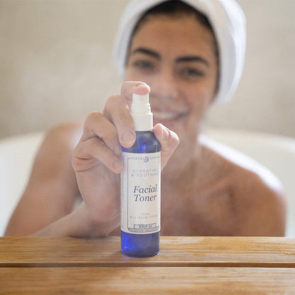 A woman joyfully spraying the Power Repair Facial Toner, while she is smiling in the bath tub.